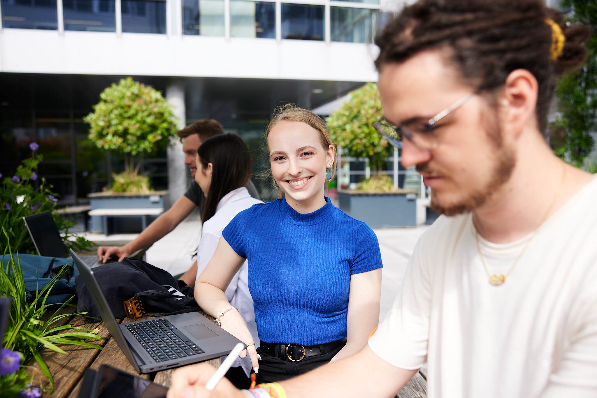 Zwei Studierende sitzen in einem Innenhof vor einem Laptop.