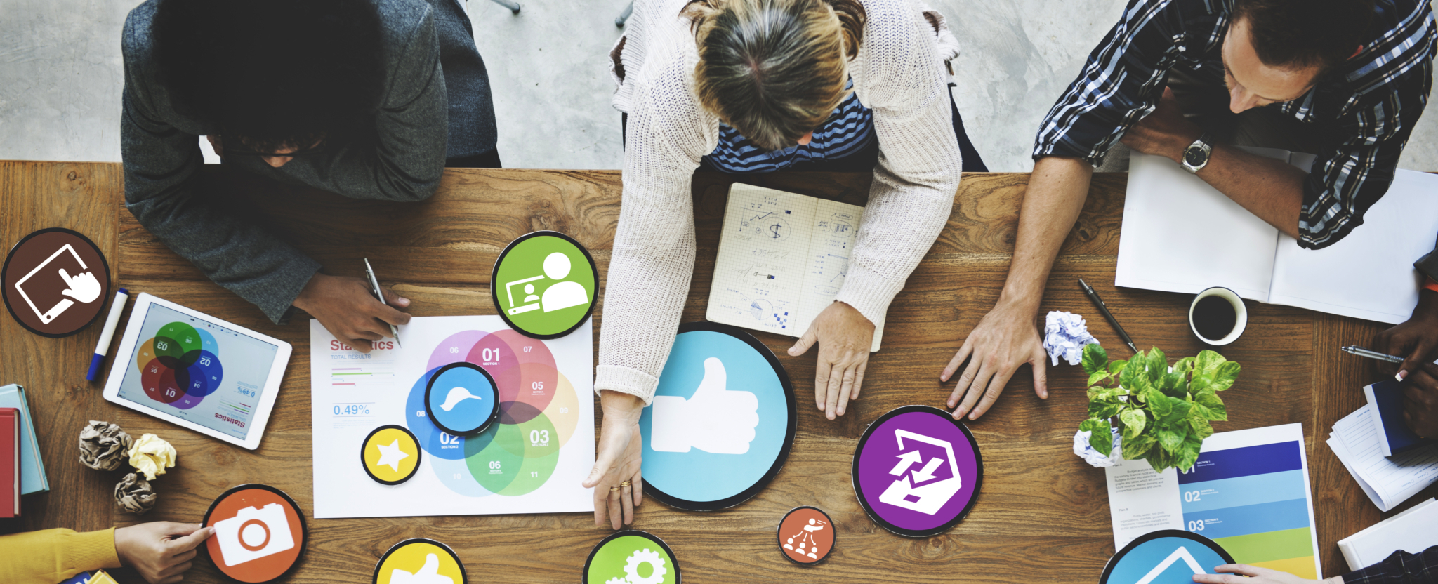 Gruppe von Menschen arbeitet gemeinsam an einem Tisch mit digitalen Symbolen, Diagrammen und Tablets